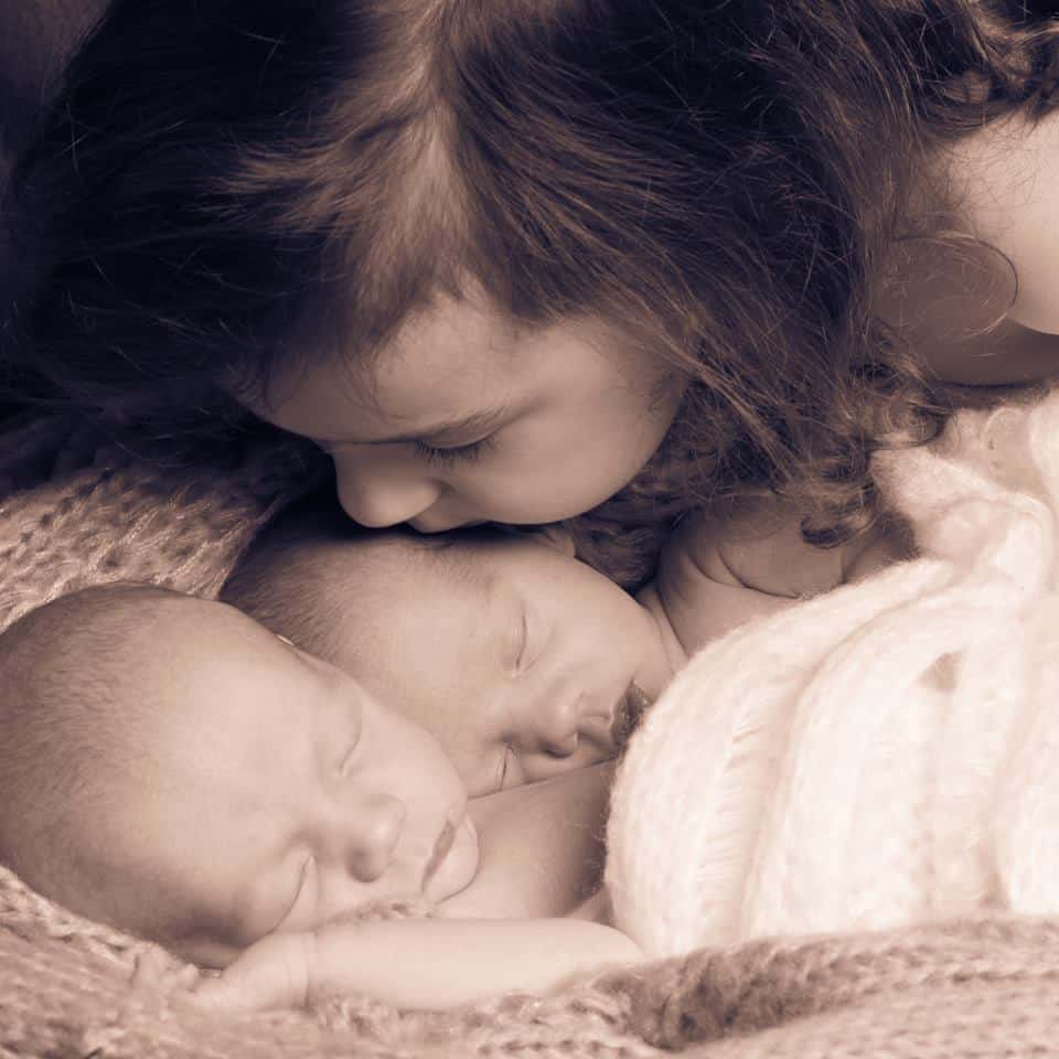 Neugeborene Zwillinge werden von ihrer Schwester geküsst. Festgehalten wurde das Foto von Familienfotografin Sissy Rauscher aus Baden